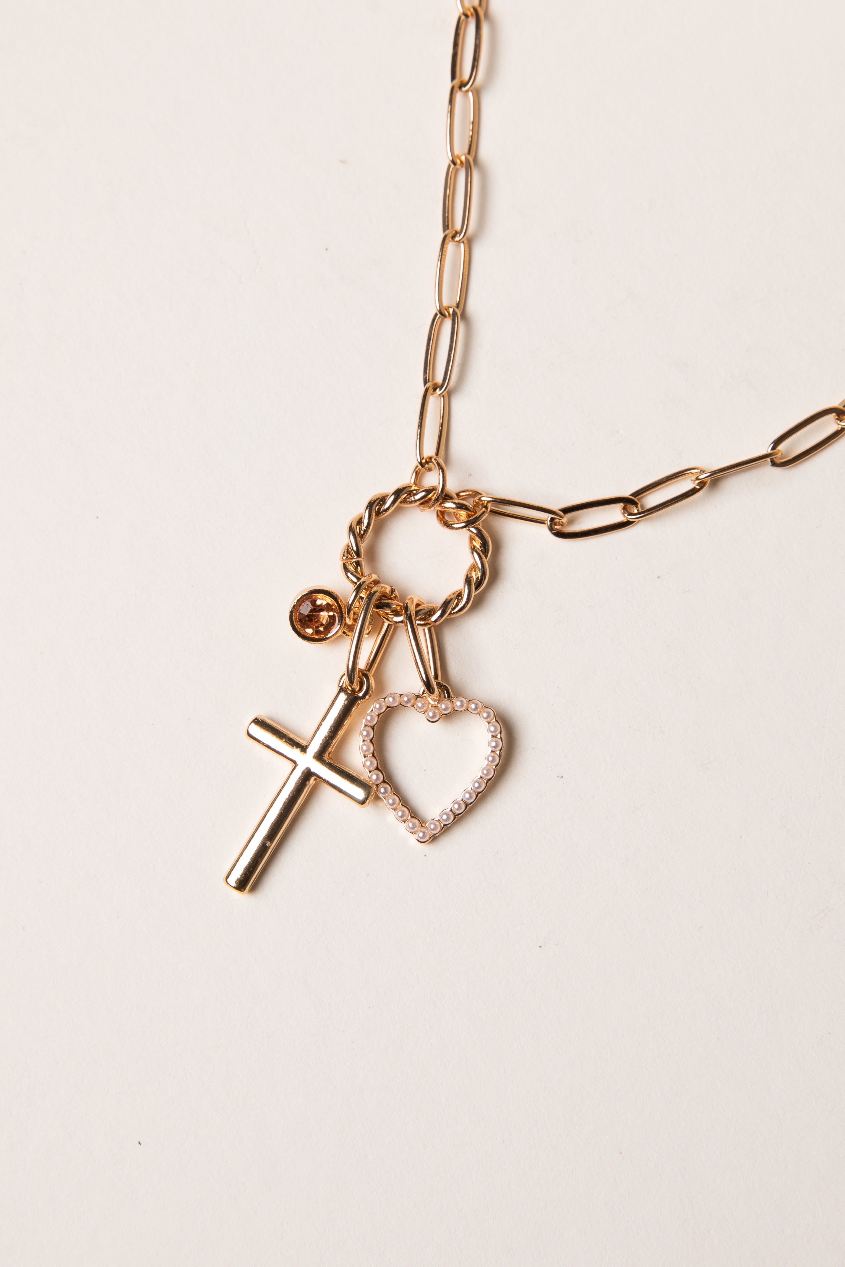 Gold necklace with cross and heart charms on a light background
