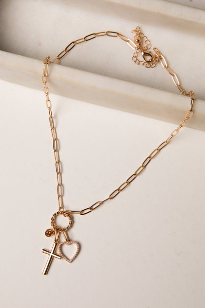 Gold chain bracelet with heart and cross charms on a light background