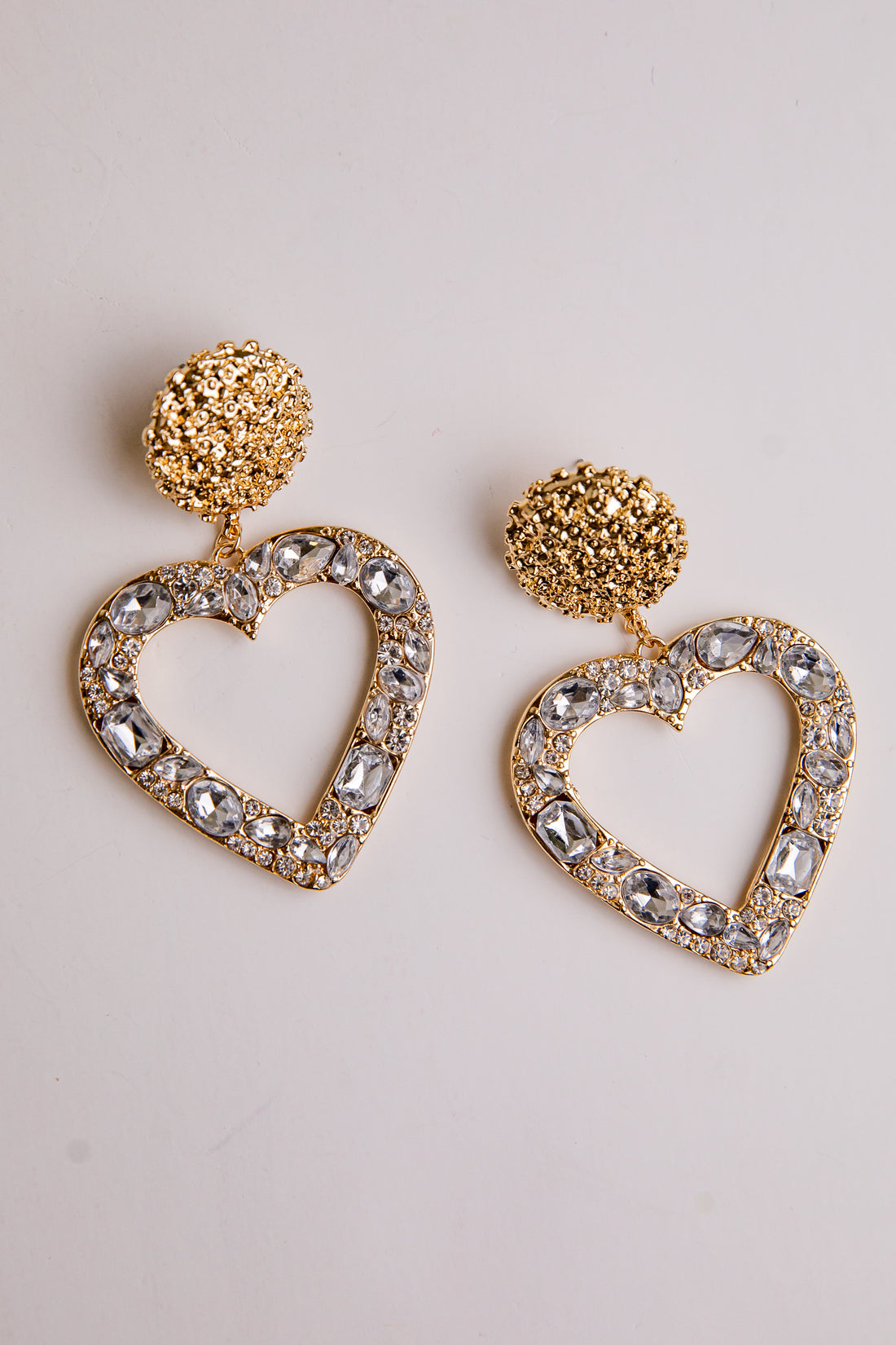 Heart-shaped earrings with gold and crystal details on a light background