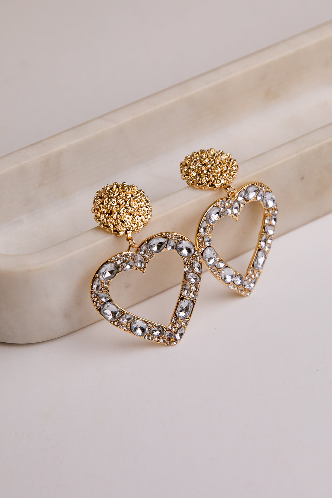 Gold heart-shaped earrings with crystal details on a light background