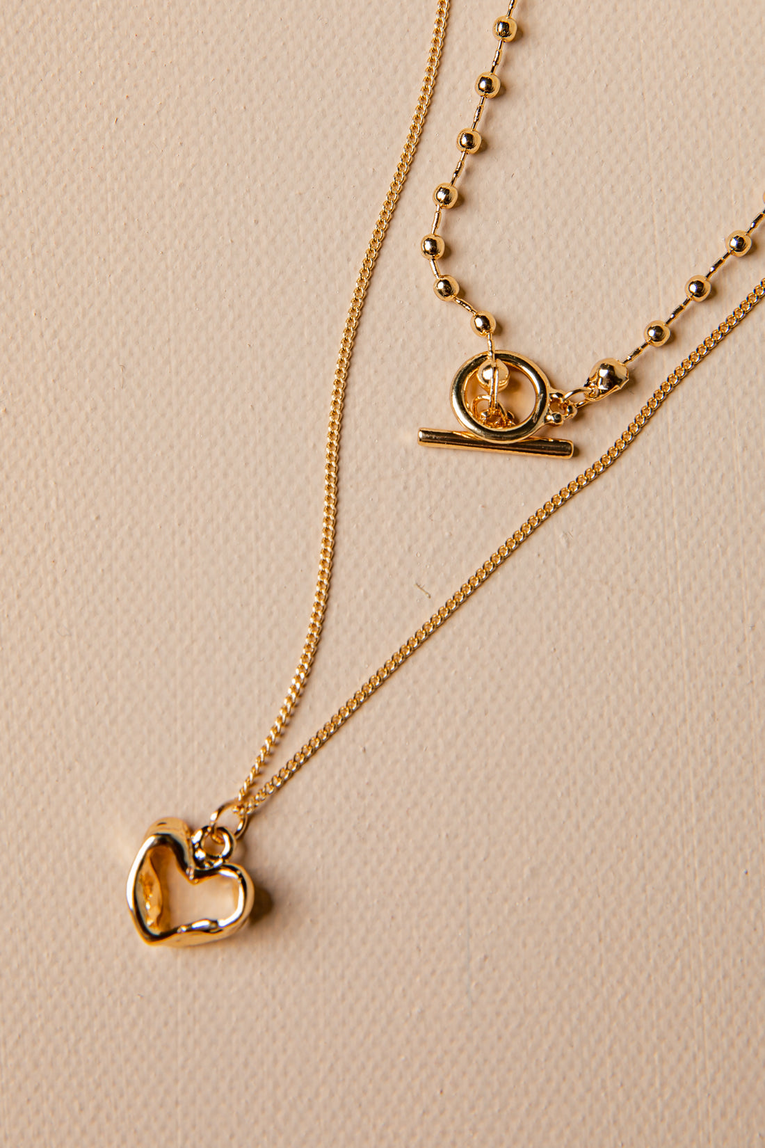 Gold necklace with heart pendant on a beige background