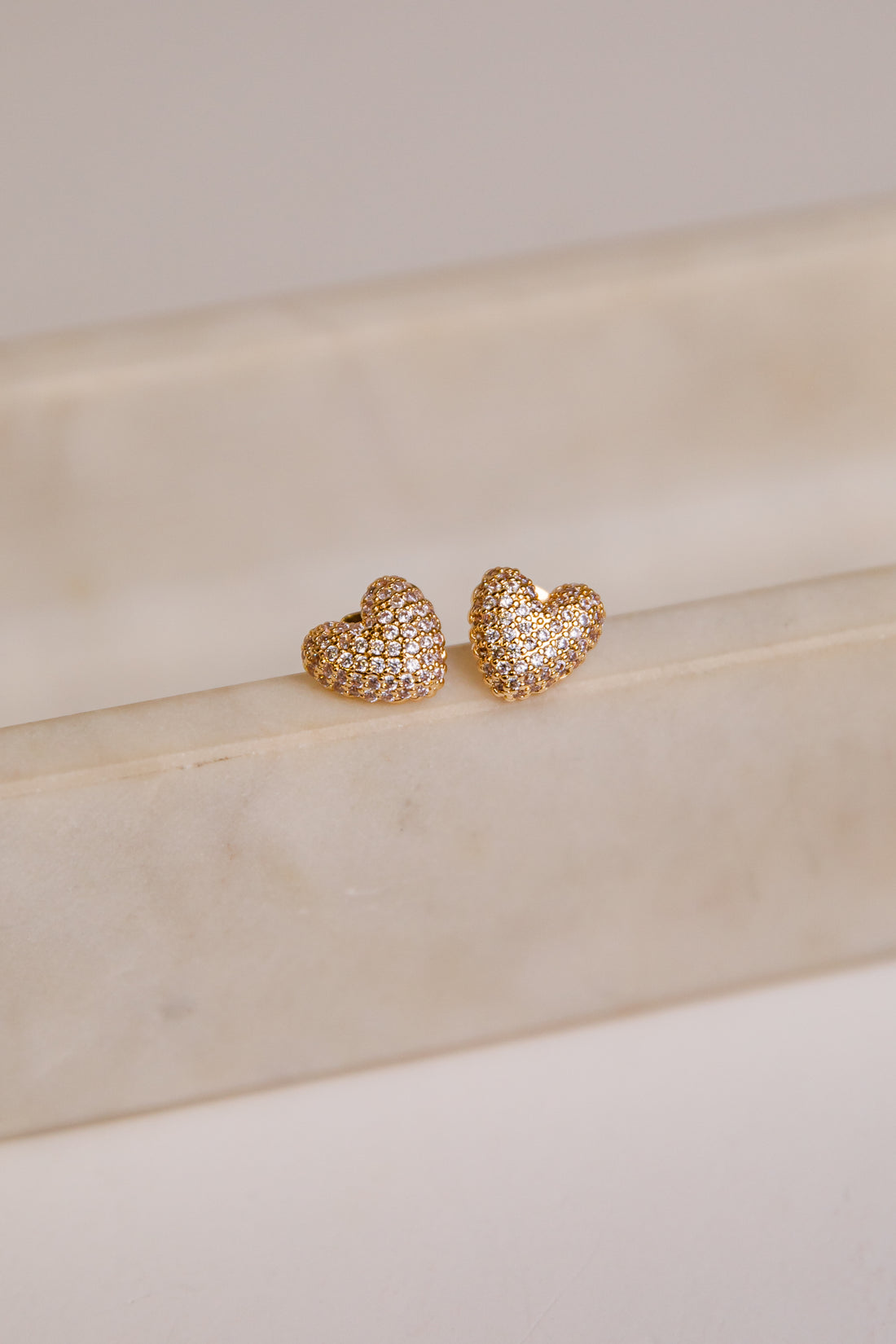 Heart-shaped gold earrings on a beige surface