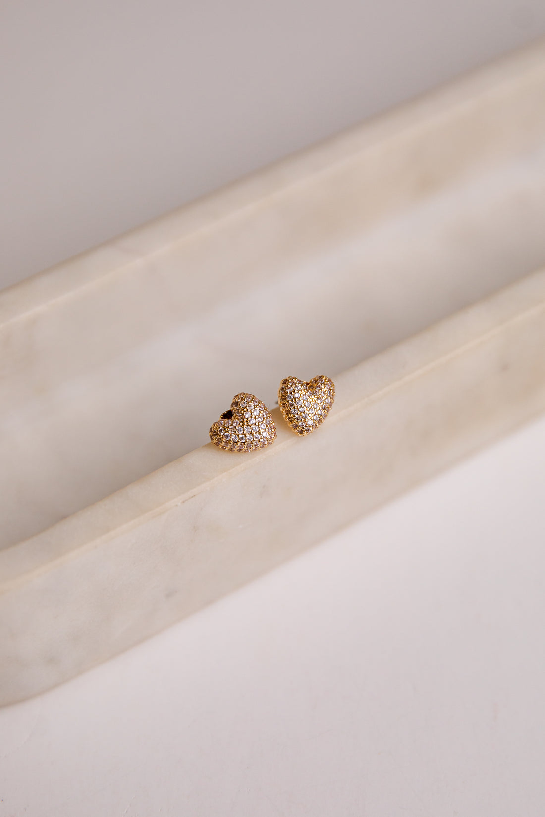 Heart-shaped gold earrings on a light beige surface
