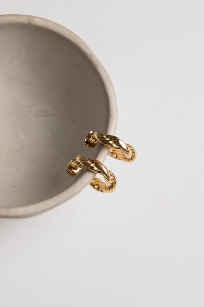 Gold ring with a unique design on a beige ceramic cup against a light gray background