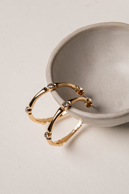 Gold hoop earrings with small stones on a beige surface