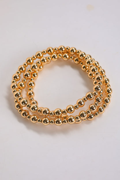 Two gold beaded bracelets on a light gray background