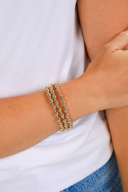 Gold beaded bracelet on a wrist with a white shirt and blue jeans background