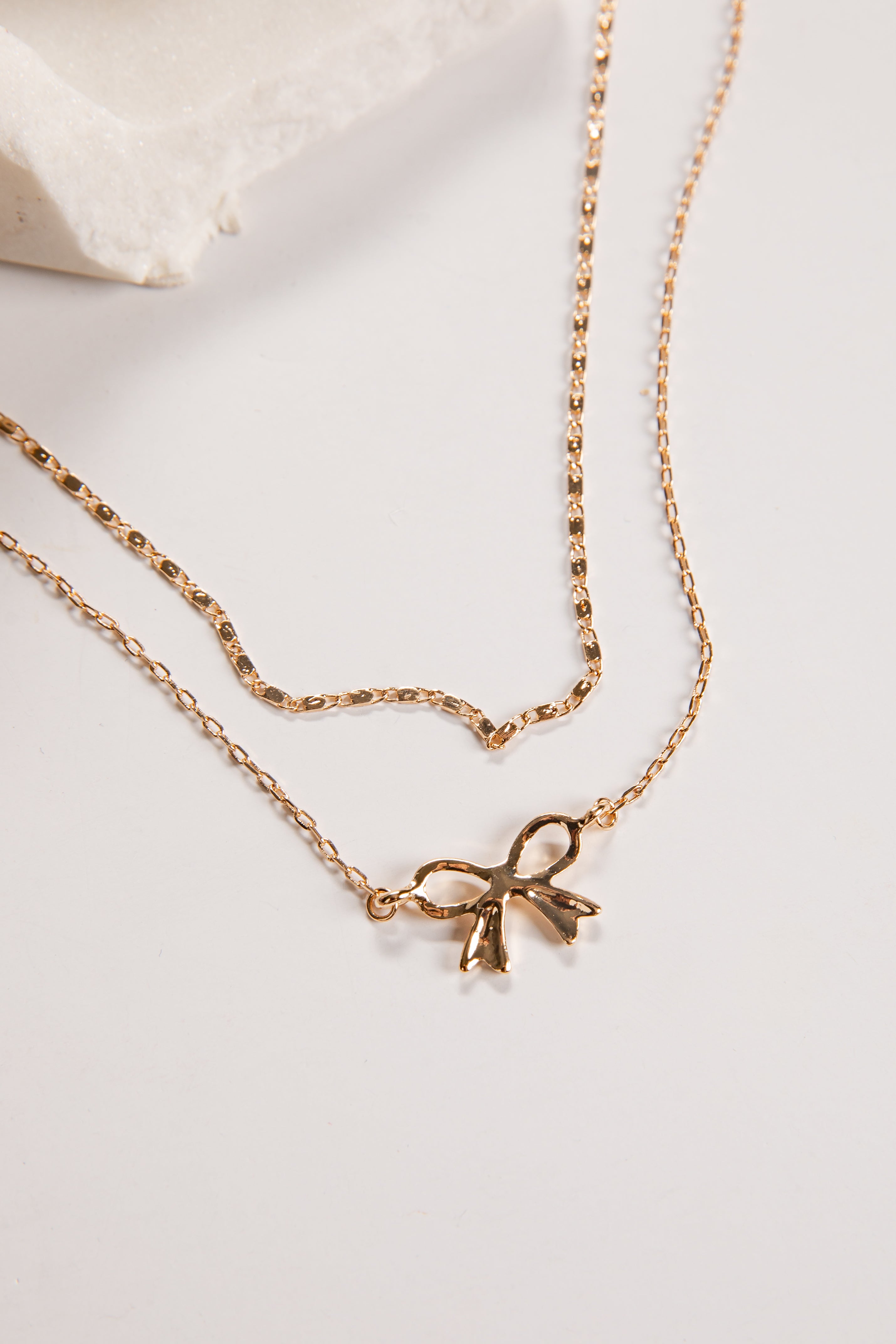 Gold necklace with a bow pendant on a light background