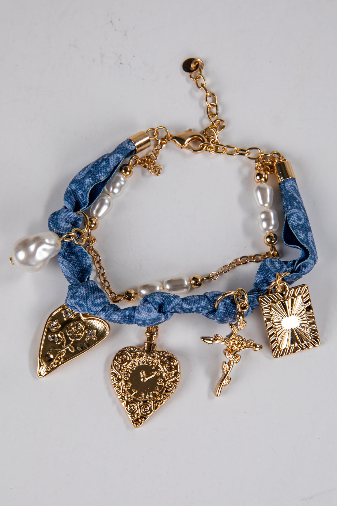 Bracelet with blue fabric wrap, gold charms, and pearl beads on a light gray background