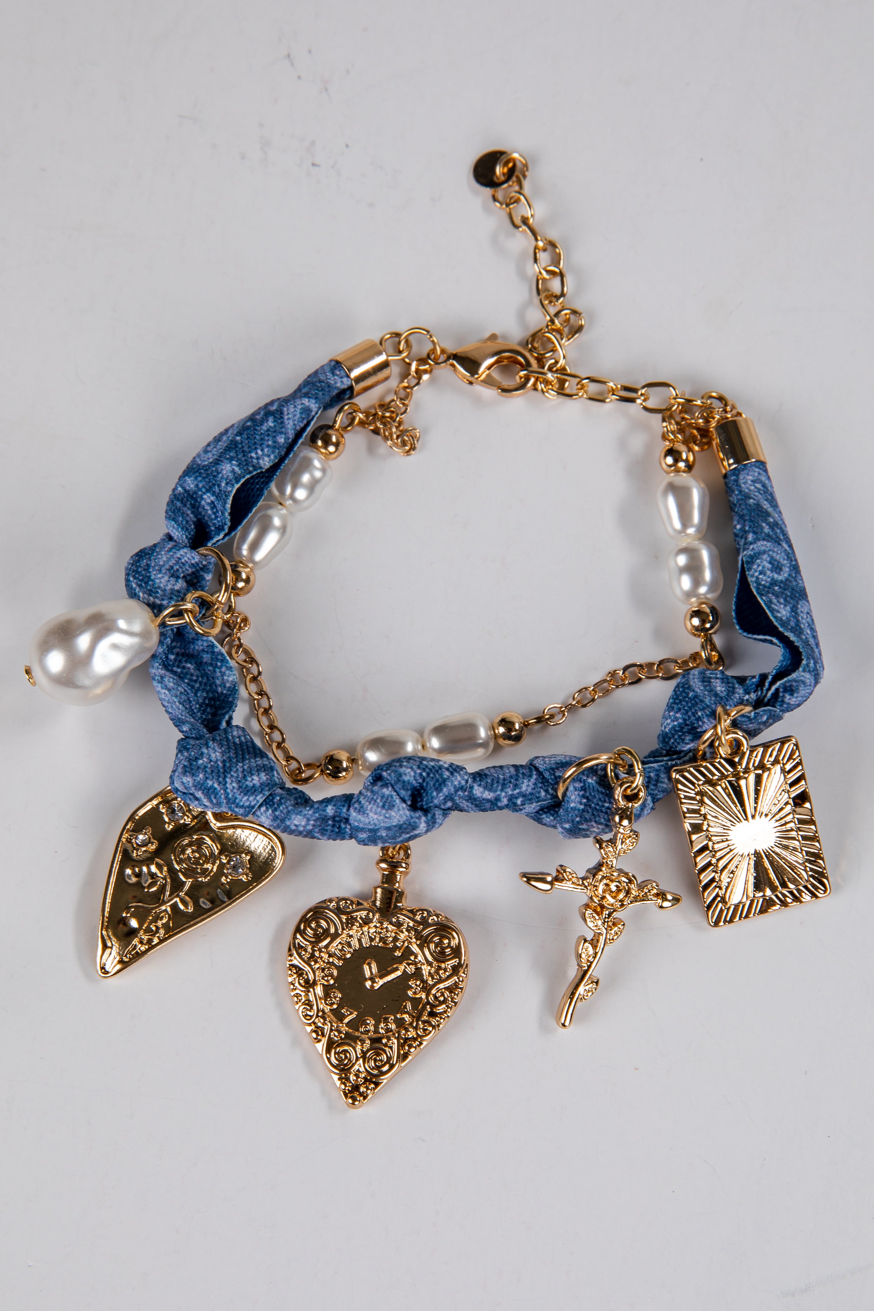 Bracelet with blue fabric wrap, gold charms, and pearl beads on a light gray background