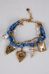 Bracelet with blue fabric wrap, gold charms, and pearl beads on a light gray background