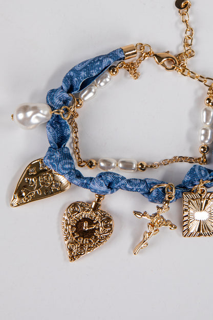 Bracelet with blue braided cord, gold charms, and pearl accents on a light gray background