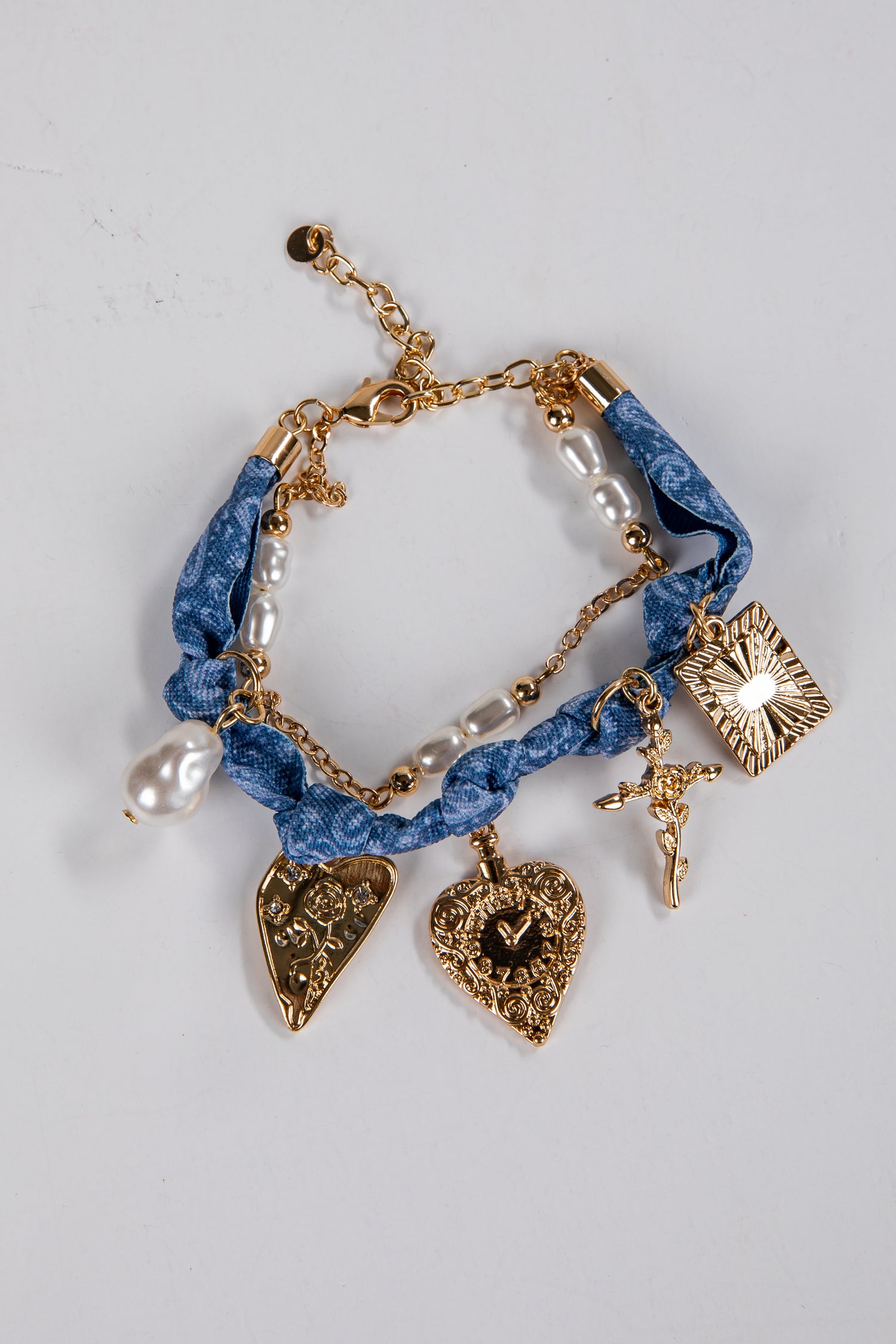 Blue braided bracelet with gold charms and pearls on a light gray background