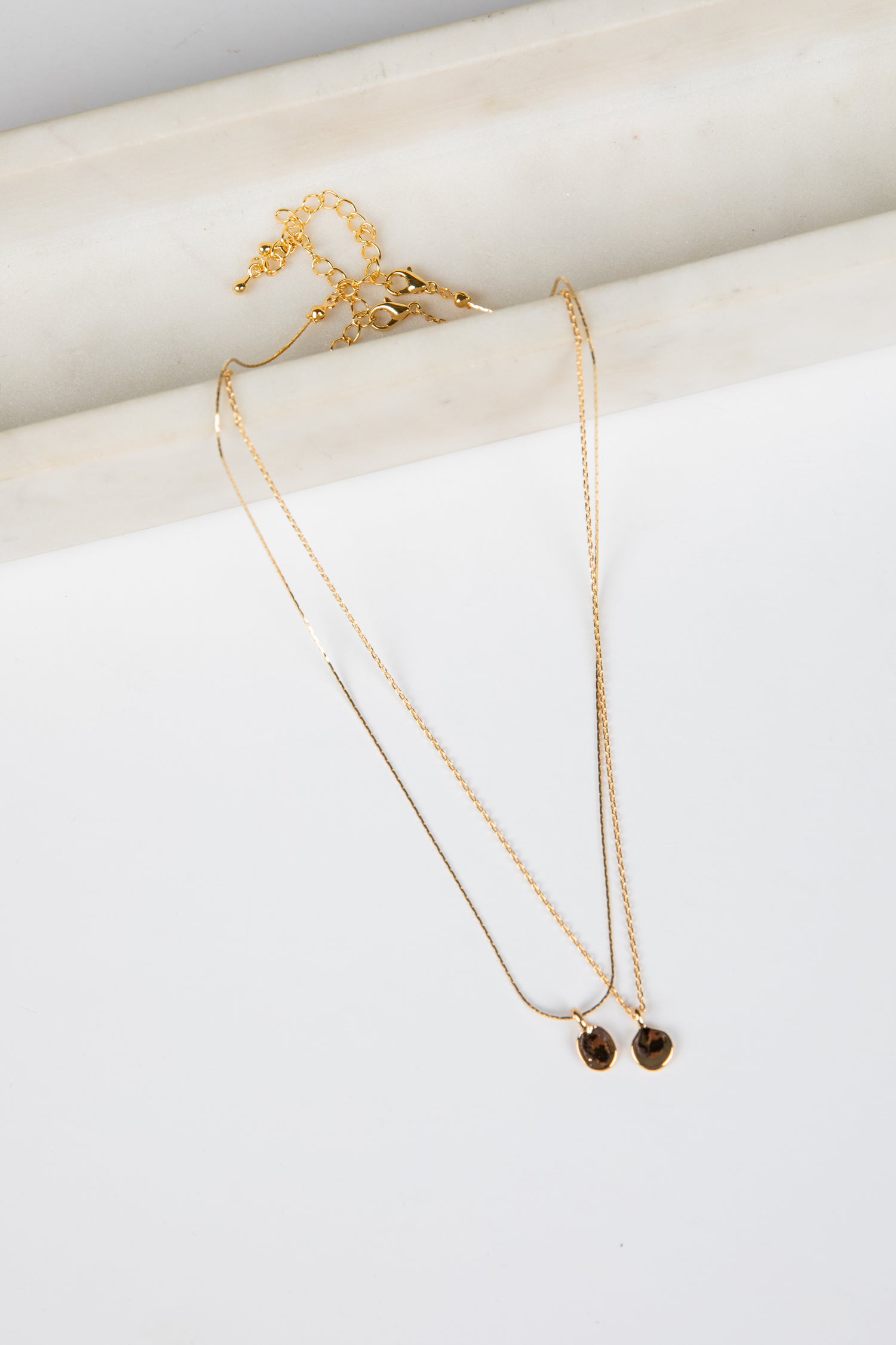 Two gold necklaces on a white surface