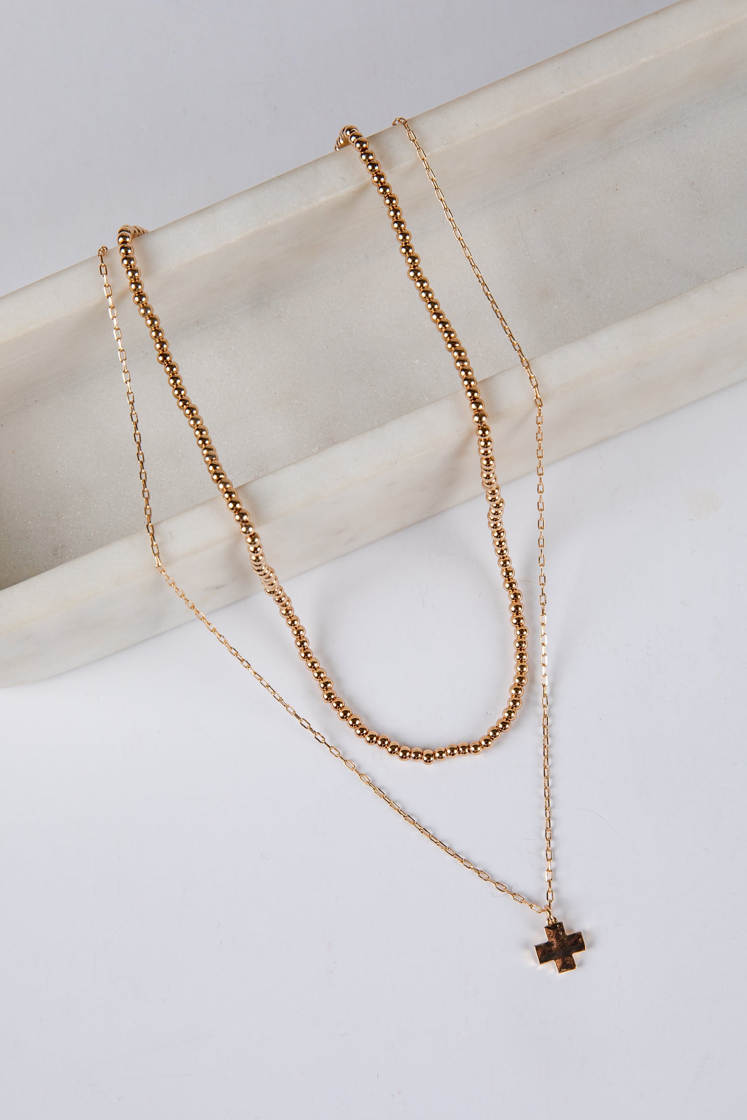 Two gold necklaces with a cross pendant on a light background