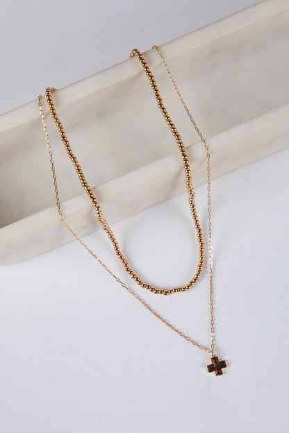 Two gold necklaces with a cross pendant on a light background