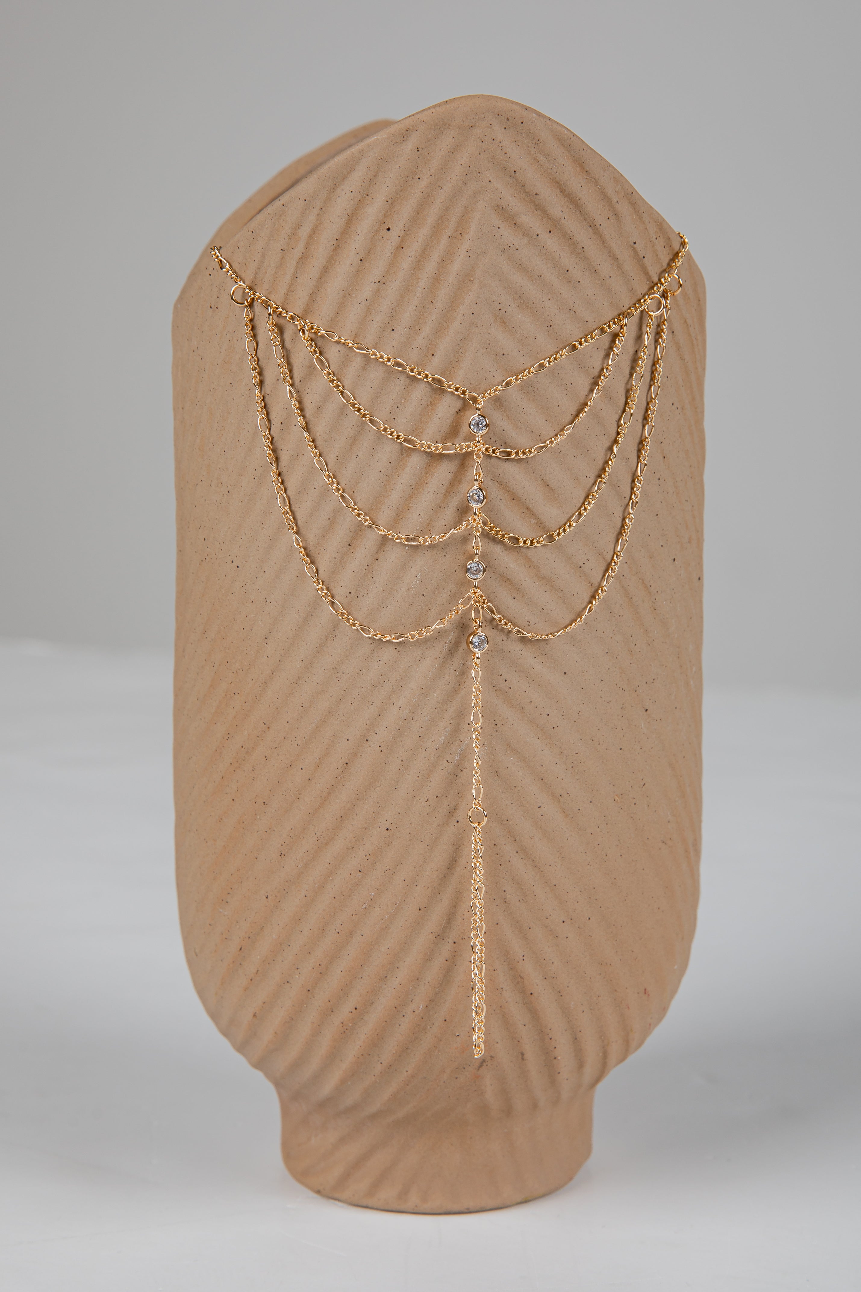Gold chain headpiece on a brown mannequin head against a gray background