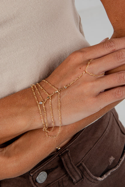 Gold bracelet and ring on a wrist with a neutral background