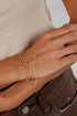 Gold bracelet and ring on a wrist with a neutral background
