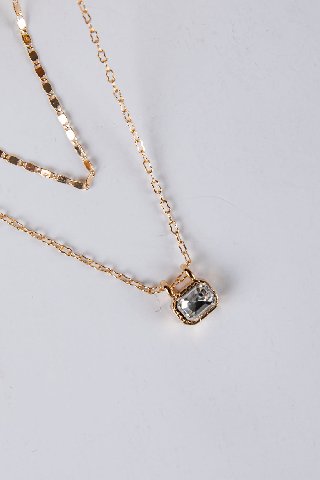 Gold necklace with a square pendant on a light gray background