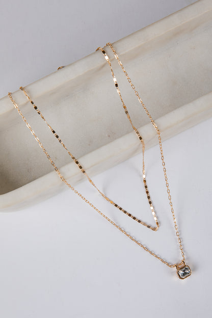 Two gold necklaces on a light gray surface