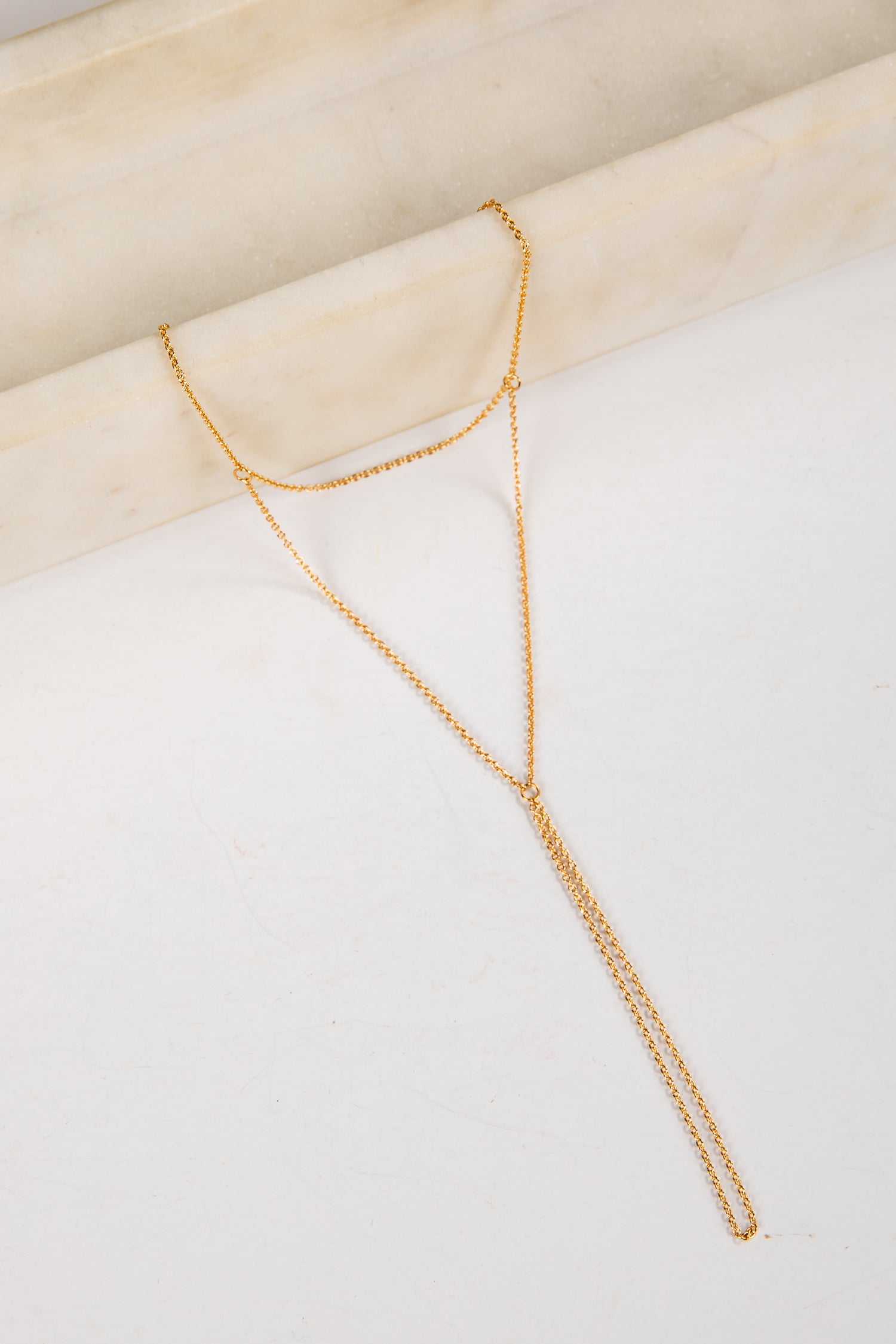Gold necklace on a white surface with a beige background