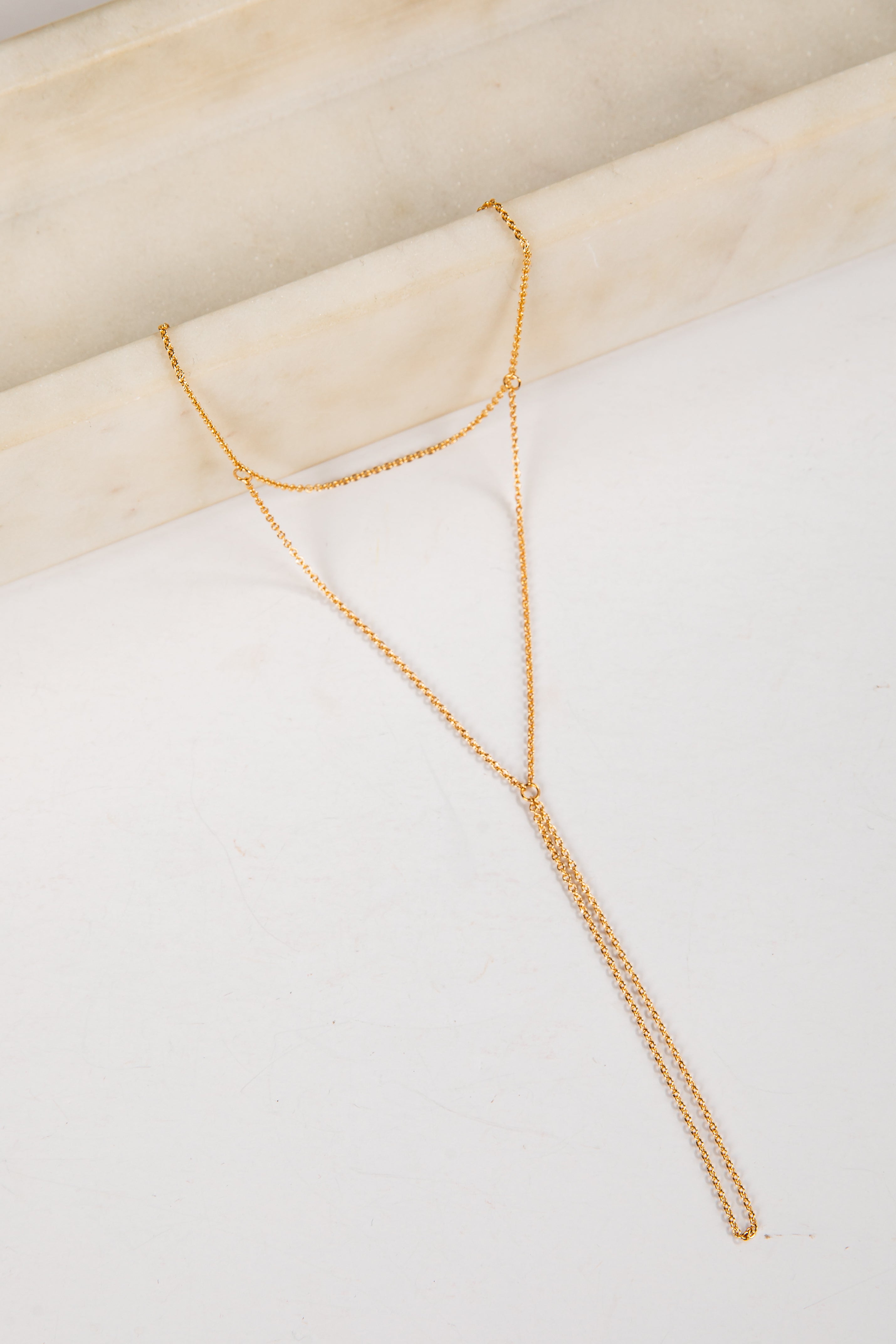 Gold necklace on a white surface with a beige background