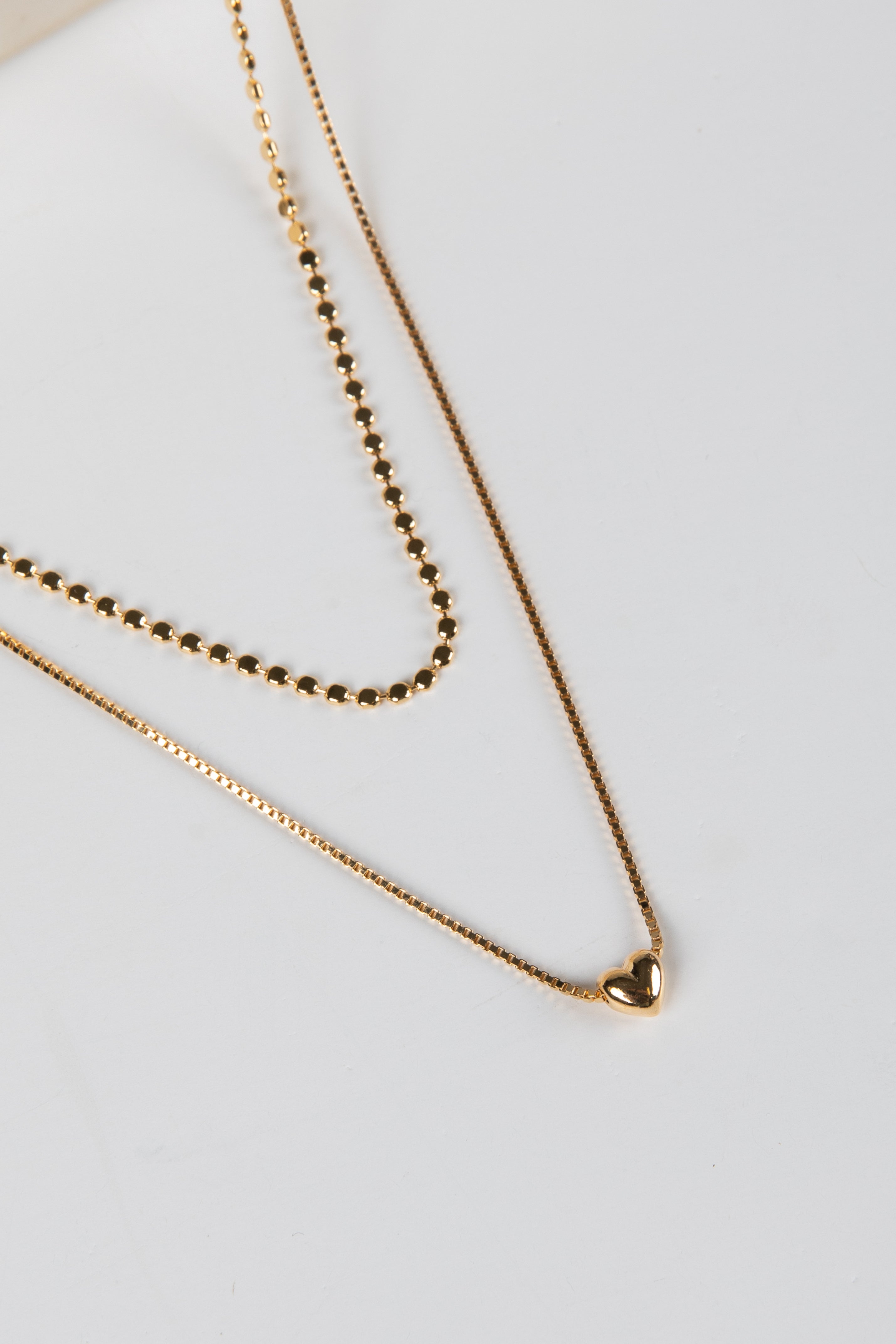 Two gold necklaces on a light gray background