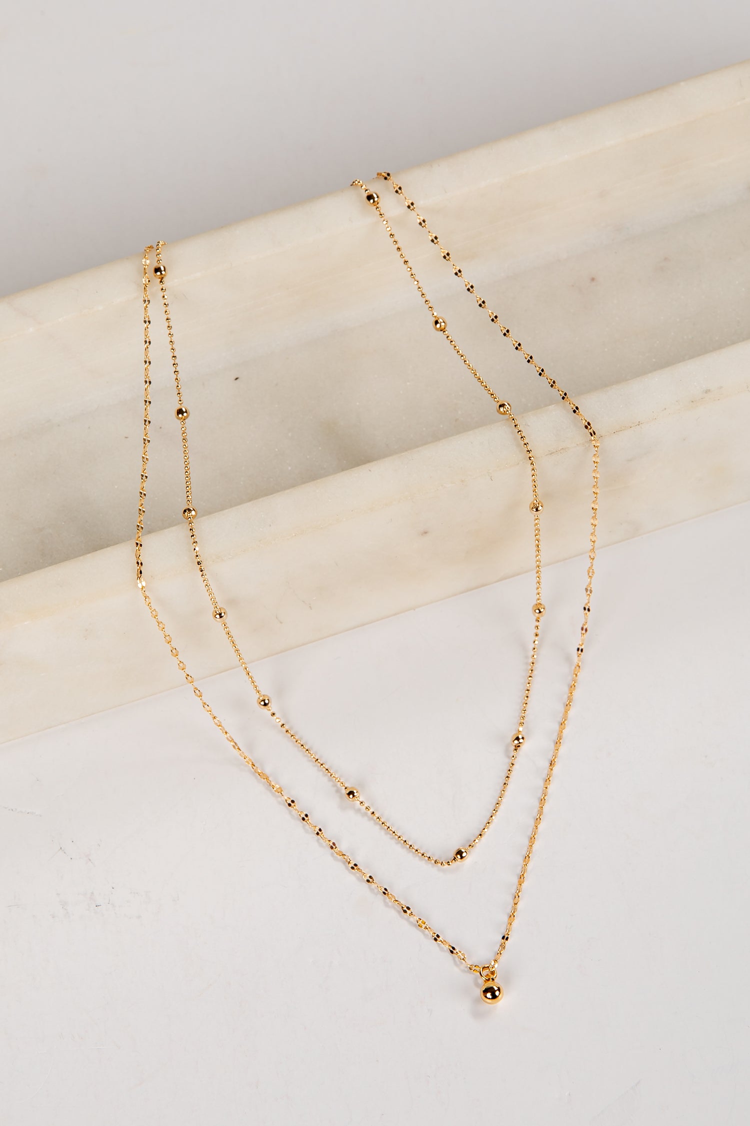 Two gold necklaces on a light wooden surface