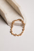 A gold-toned bracelet with multiple oval clear gemstones, displayed on a light cream stone riser against a clean off-white background.