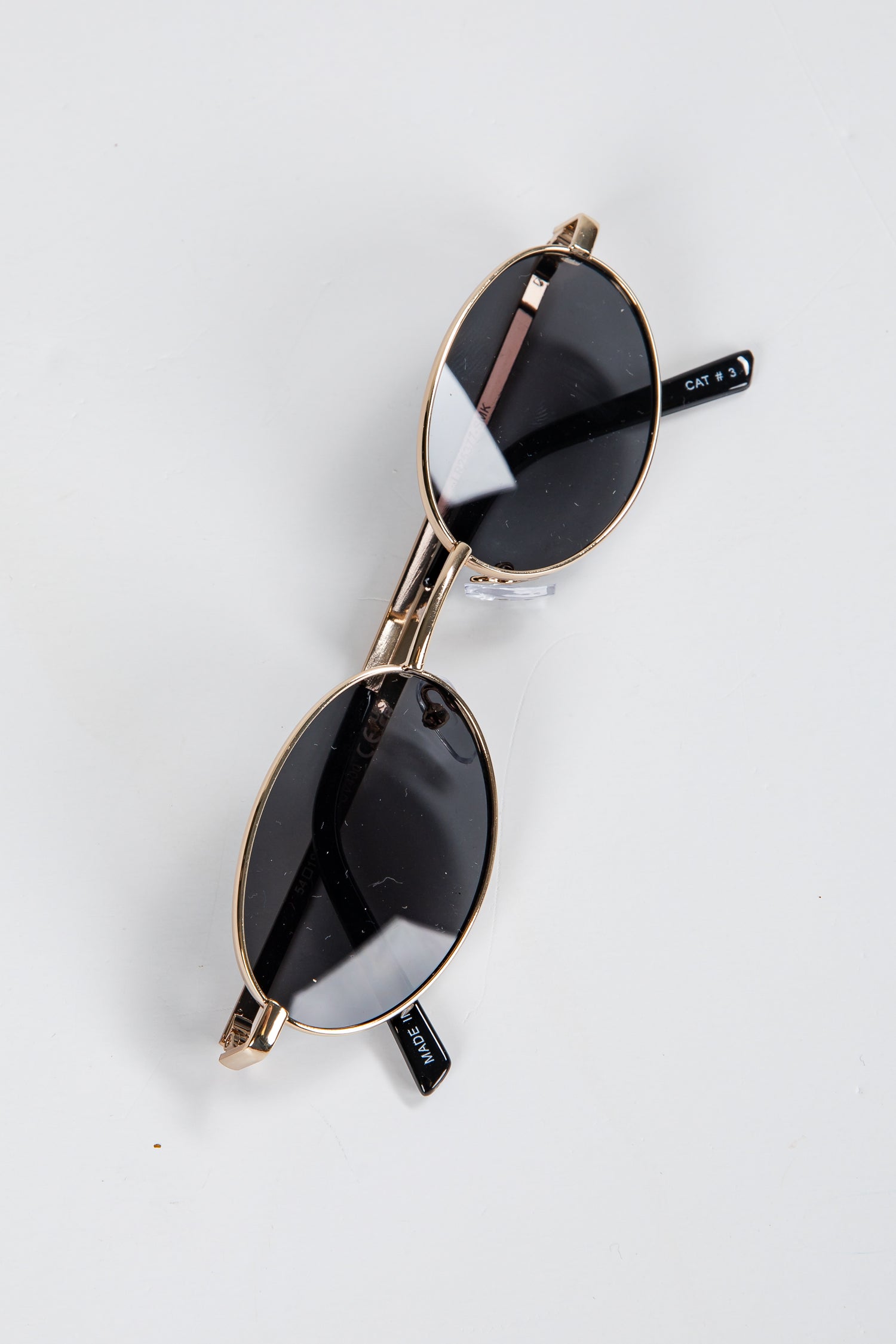 Pair of sunglasses with gold frame and black lenses on a white background