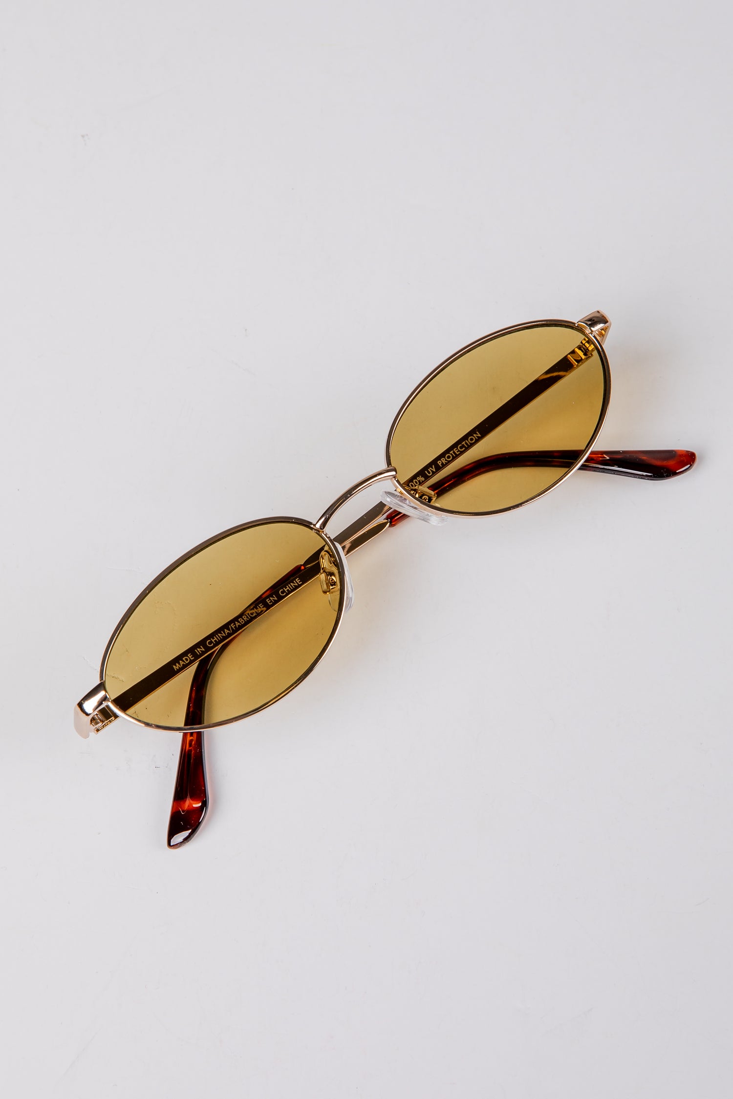 Gold-framed sunglasses with amber lenses on a light gray background