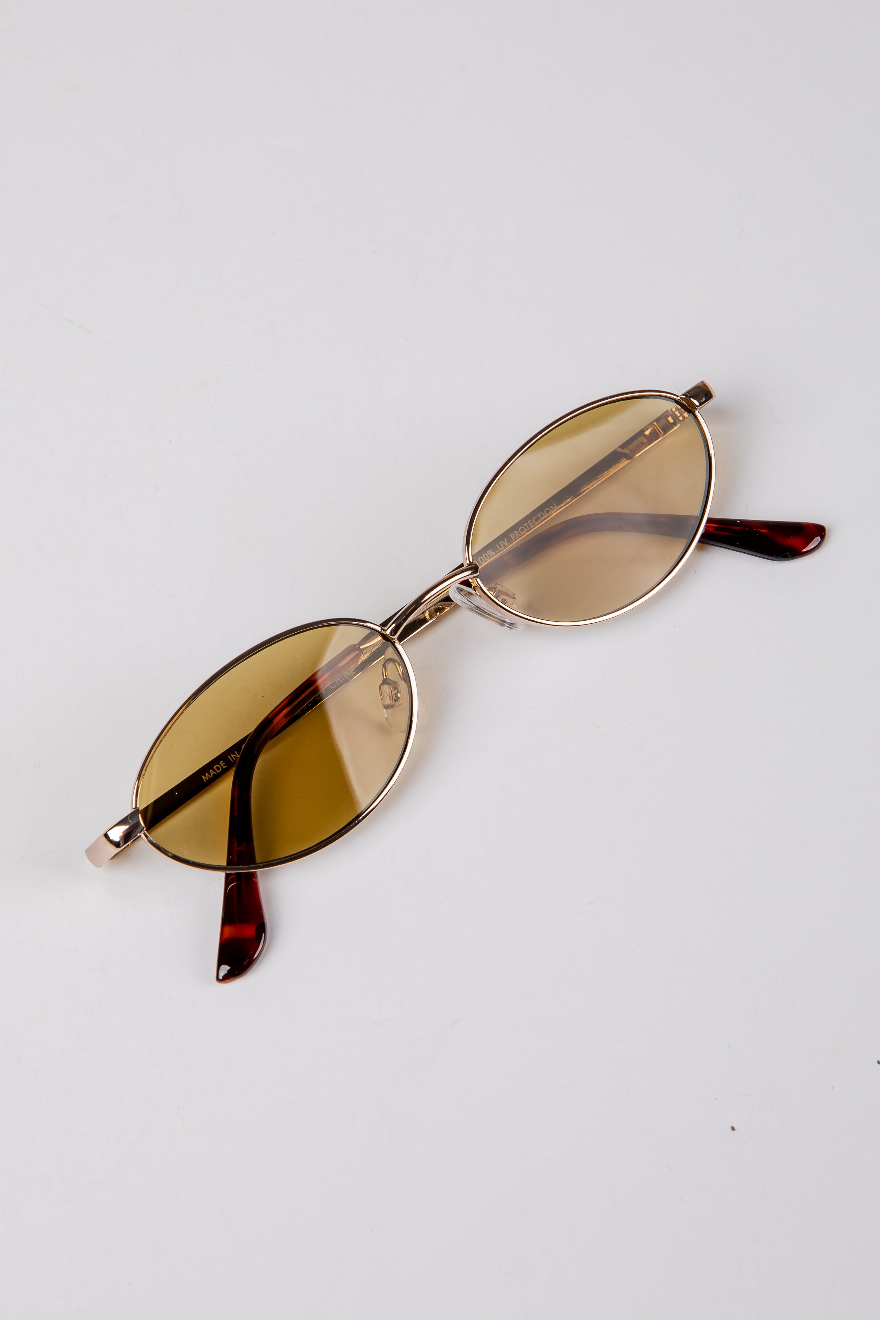 Round sunglasses with gold frame and amber lenses on a light gray background