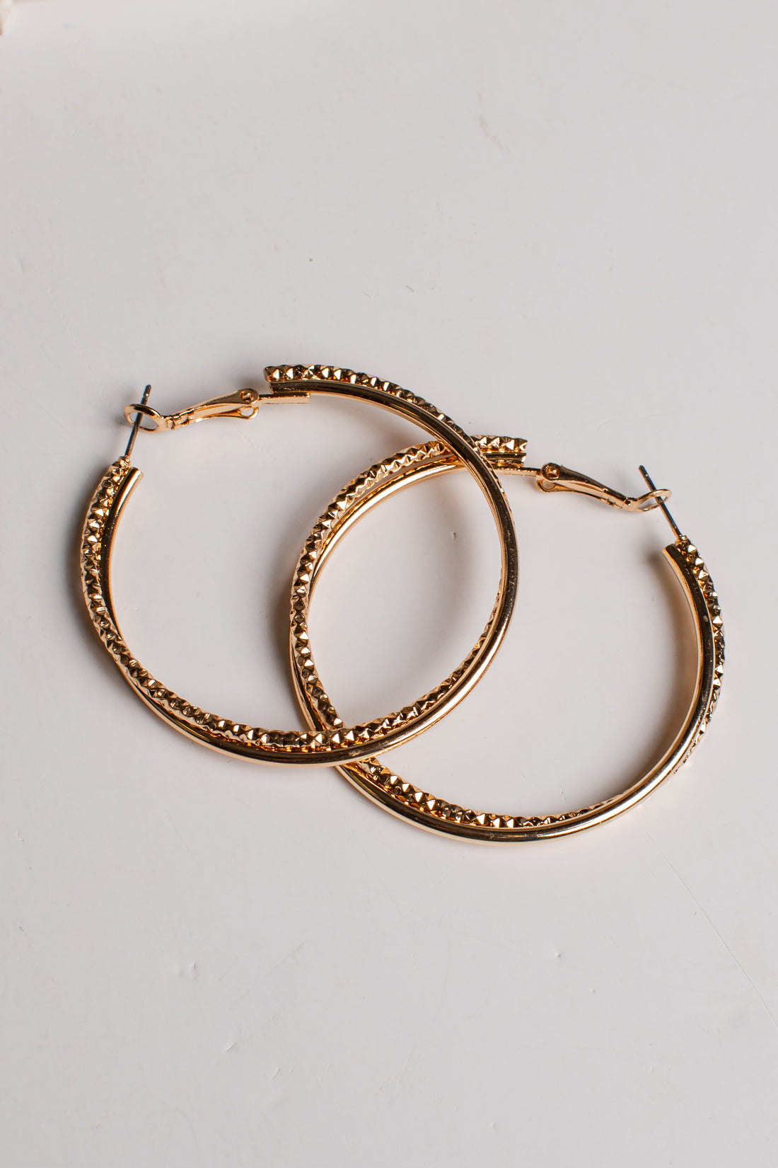 A pair of gold-tone hoop earrings with a textured, beaded outer edge and solid inner bands, displayed on a clean white background.