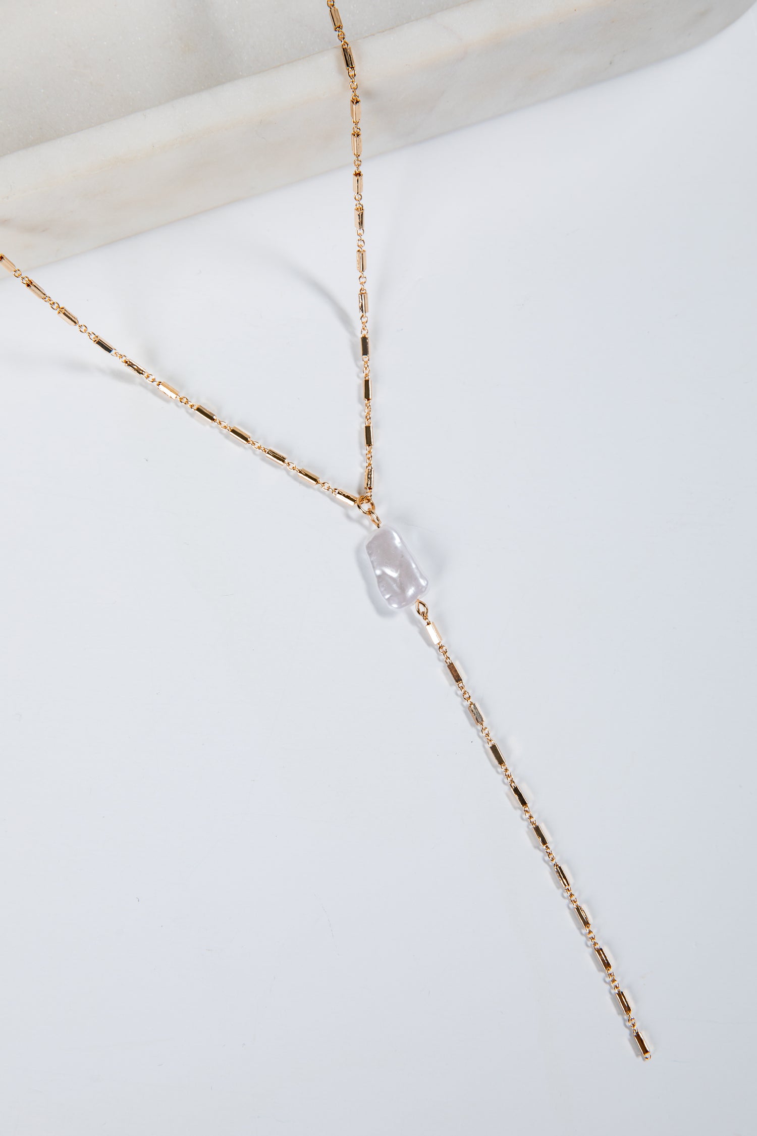 Gold necklace with a clear pendant on a white surface