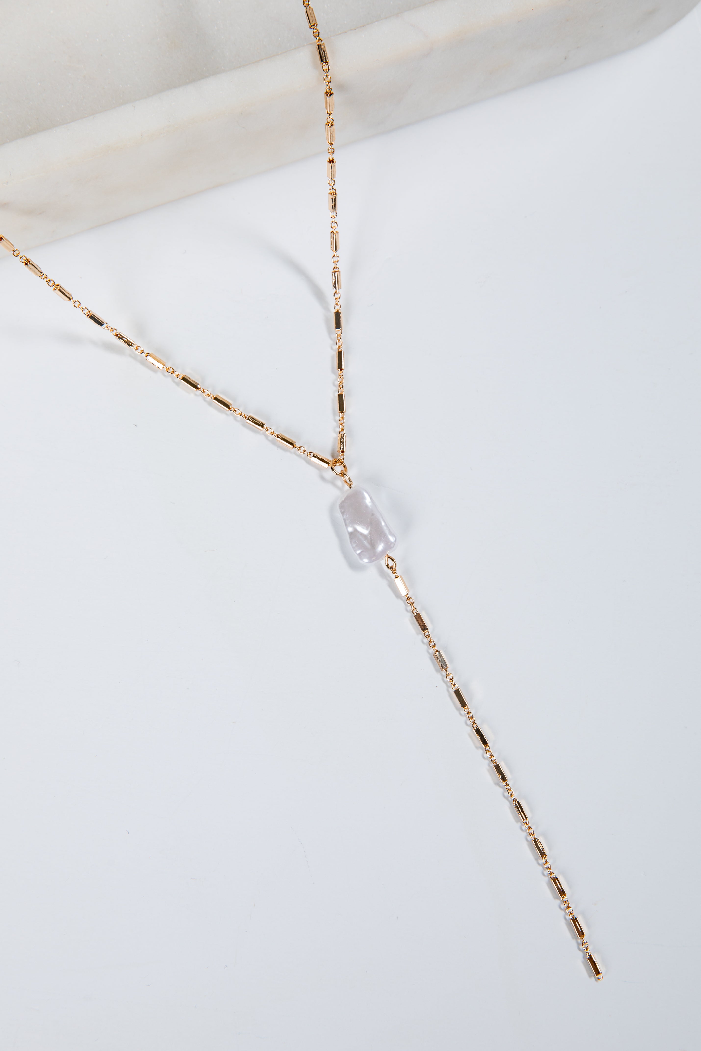 Gold necklace with a clear pendant on a white surface