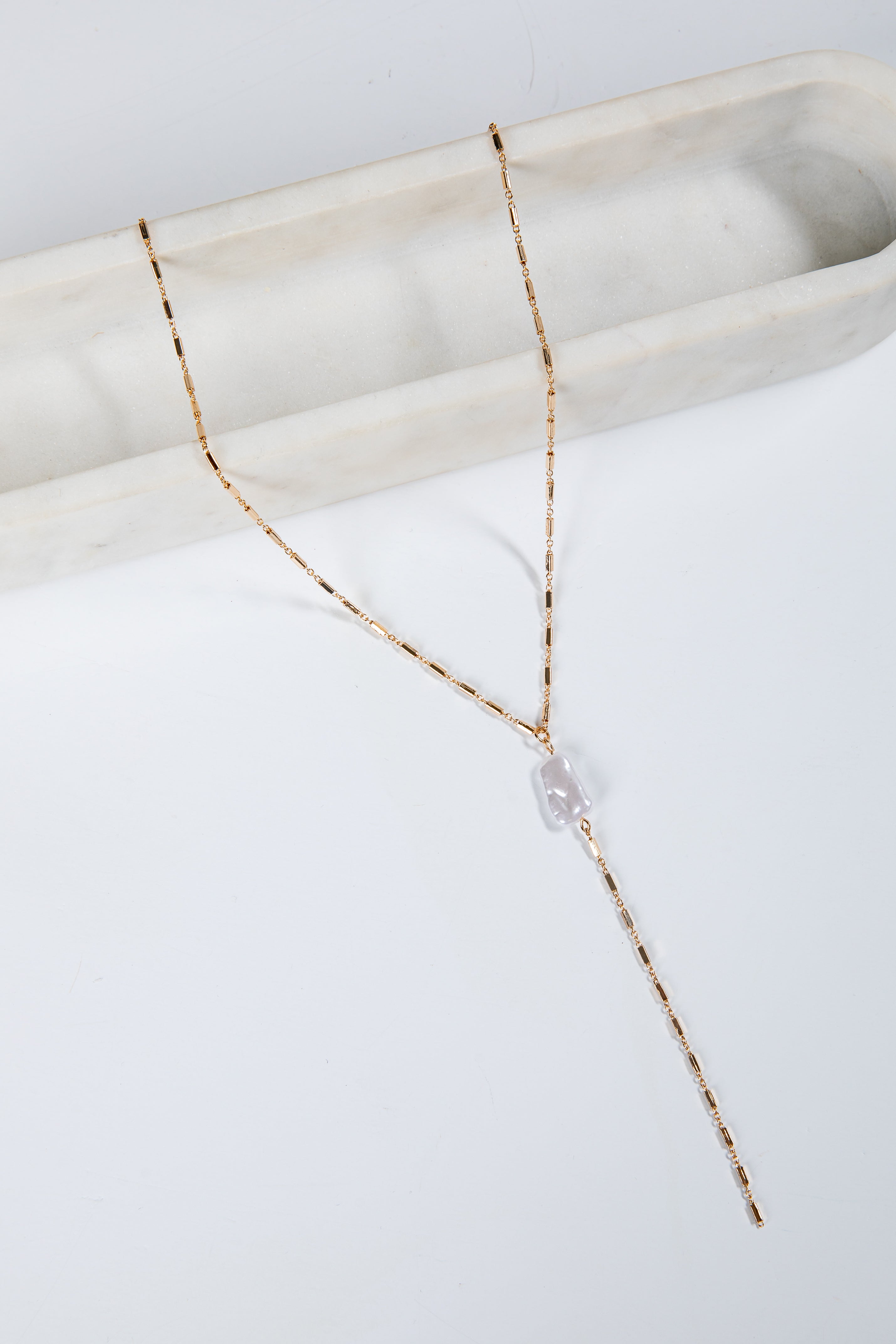 Delicate gold necklace with a pearl pendant on a white marble surface