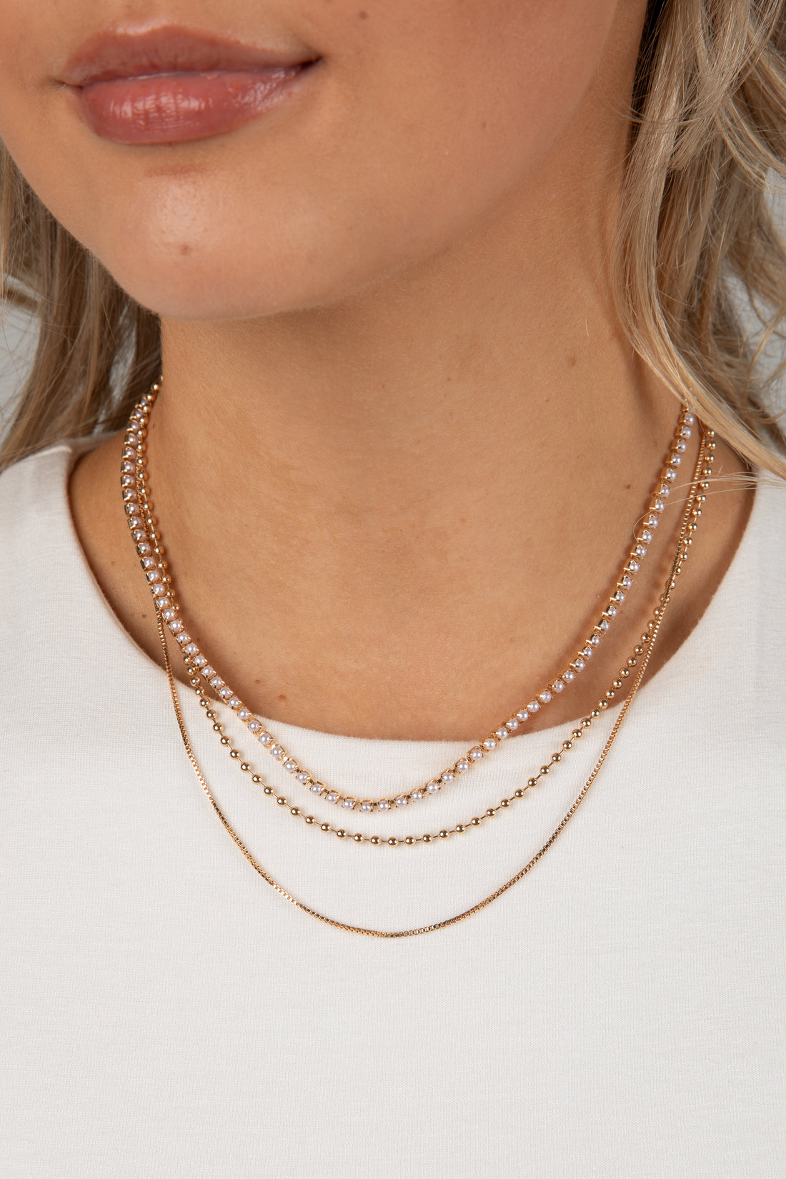 Close-up of a person wearing two gold necklaces on a plain background