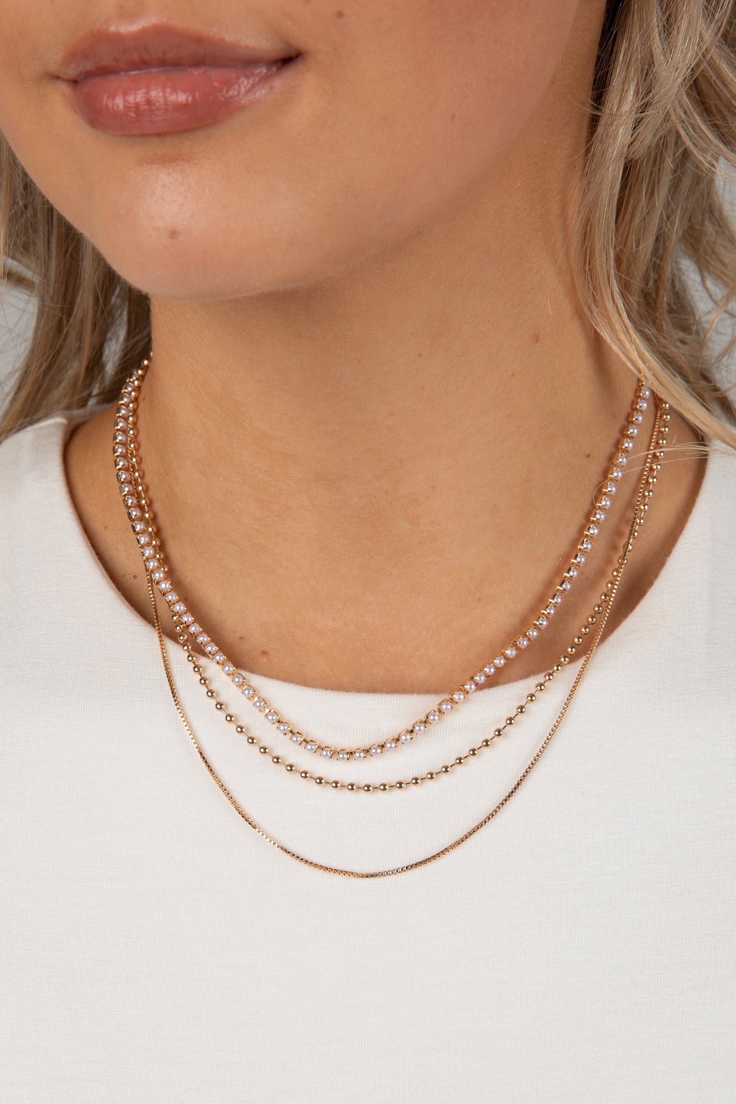 Close-up of a person wearing two gold necklaces on a plain background