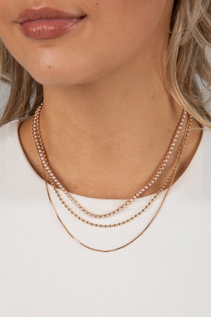 Close-up of a person wearing two gold necklaces on a plain background
