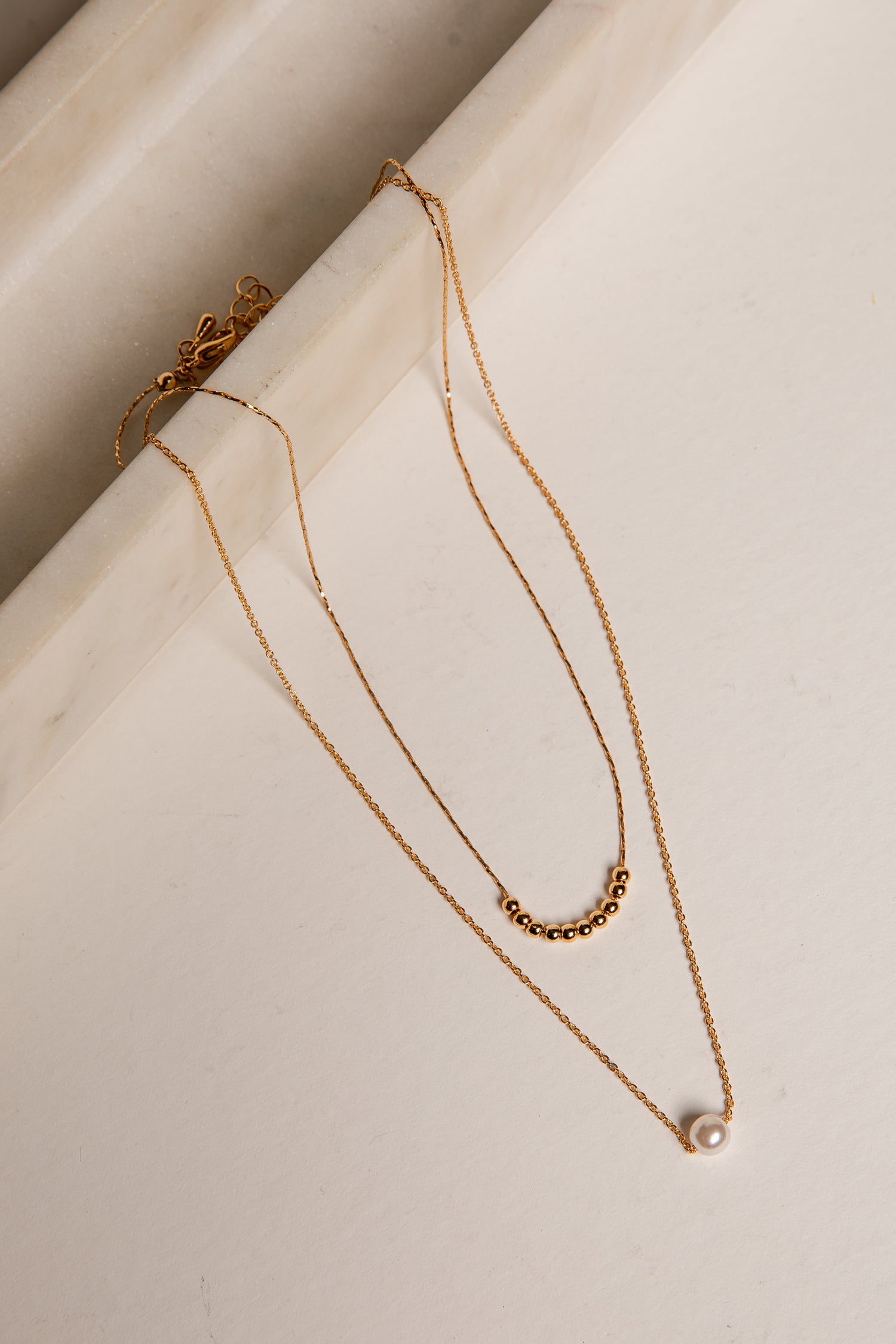Gold necklace with a pearl pendant on a light surface