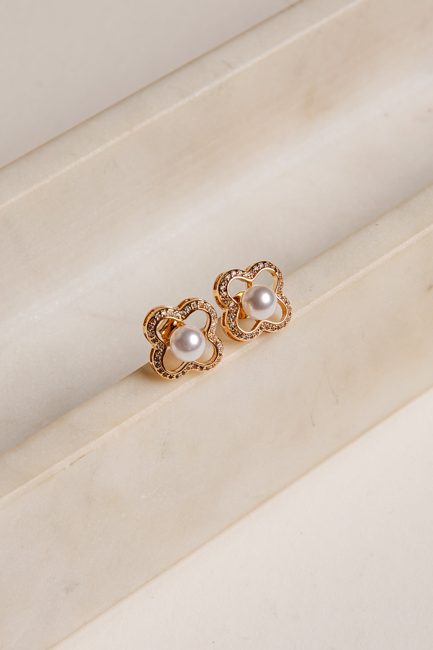 Gold earrings with pearl-like stones on a beige surface