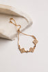 A gold-toned adjustable chain bracelet with four flower-shaped charms set with clear stones, displayed on a light beige stone slab against a white background.