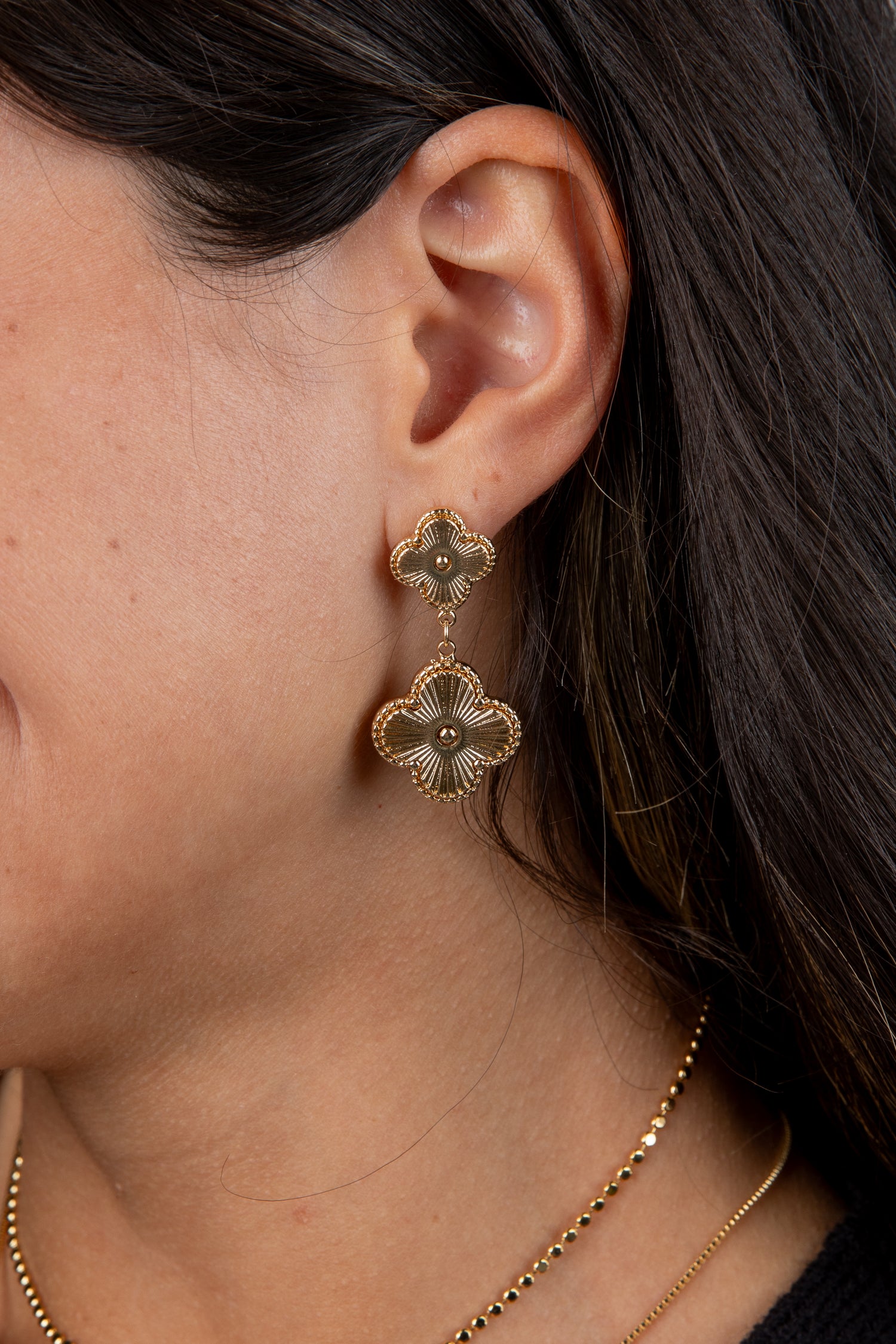 Close-up of a person wearing gold floral earrings with dark hair.