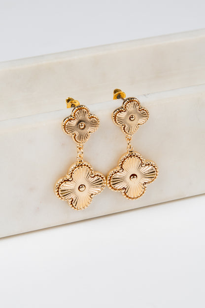 Gold floral earrings on a white marble surface
