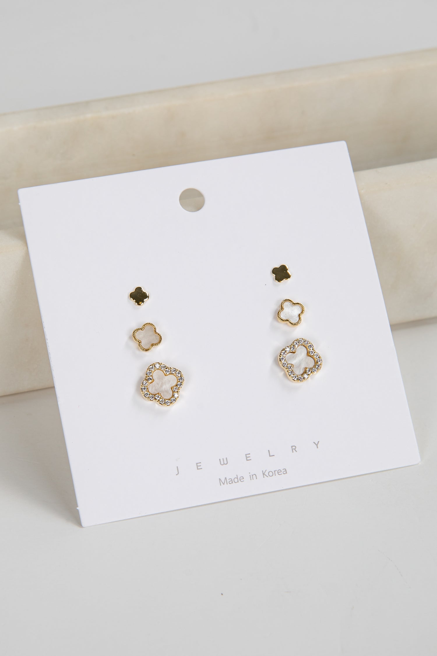 Gold floral earrings on a white jewelry card with a beige background