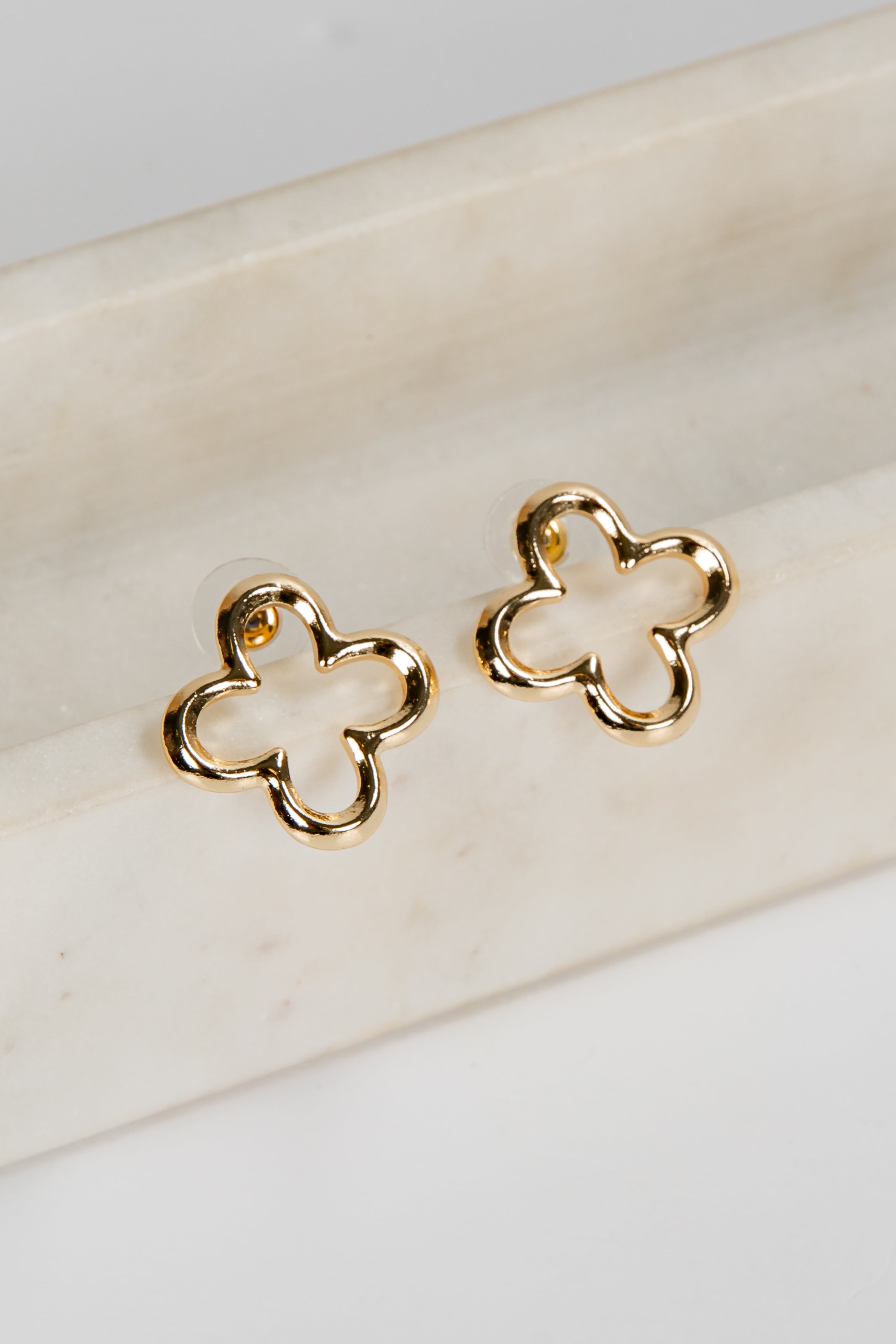 Gold four-leaf clover earrings on a marble surface
