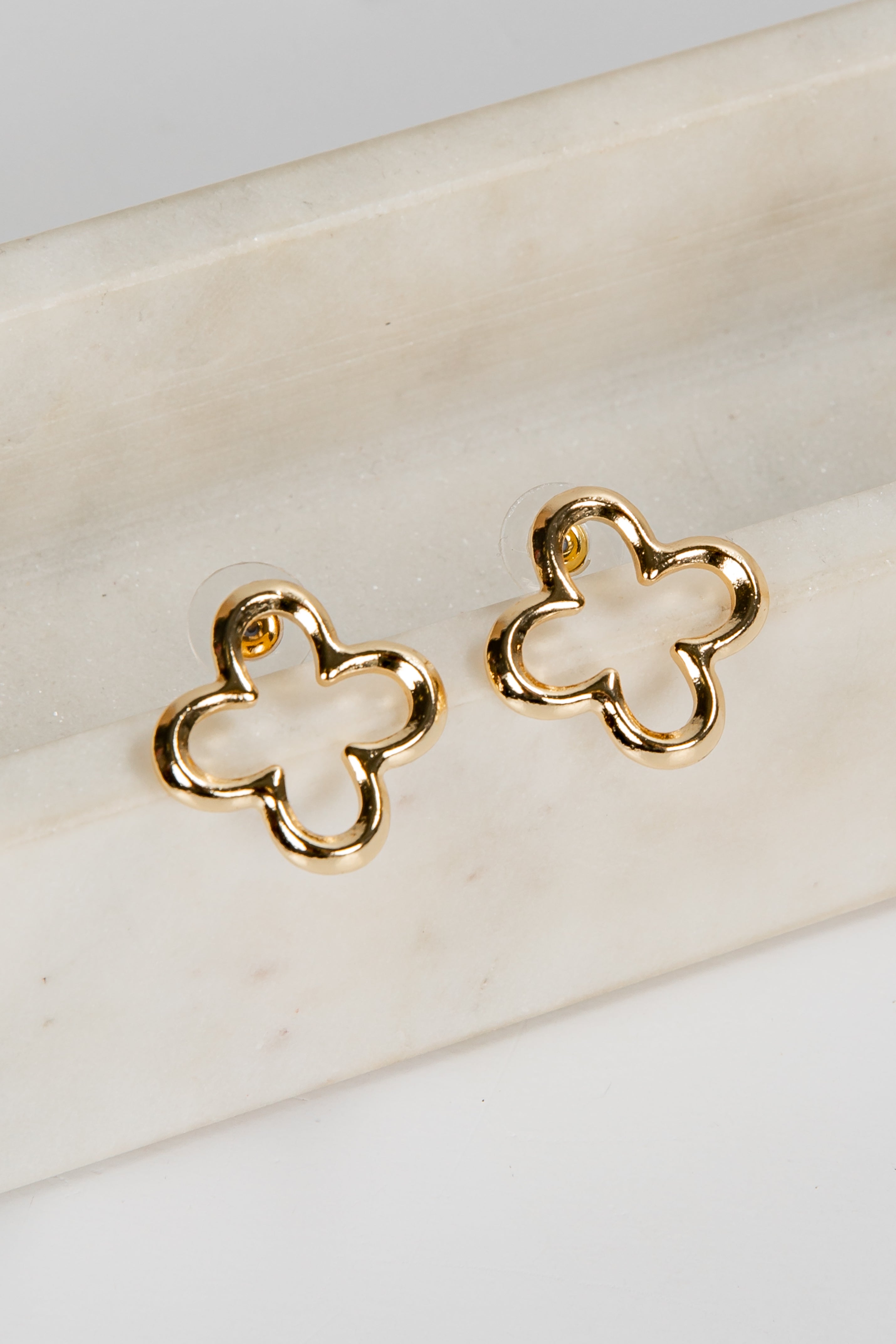 Gold four-leaf clover earrings on a white marble surface