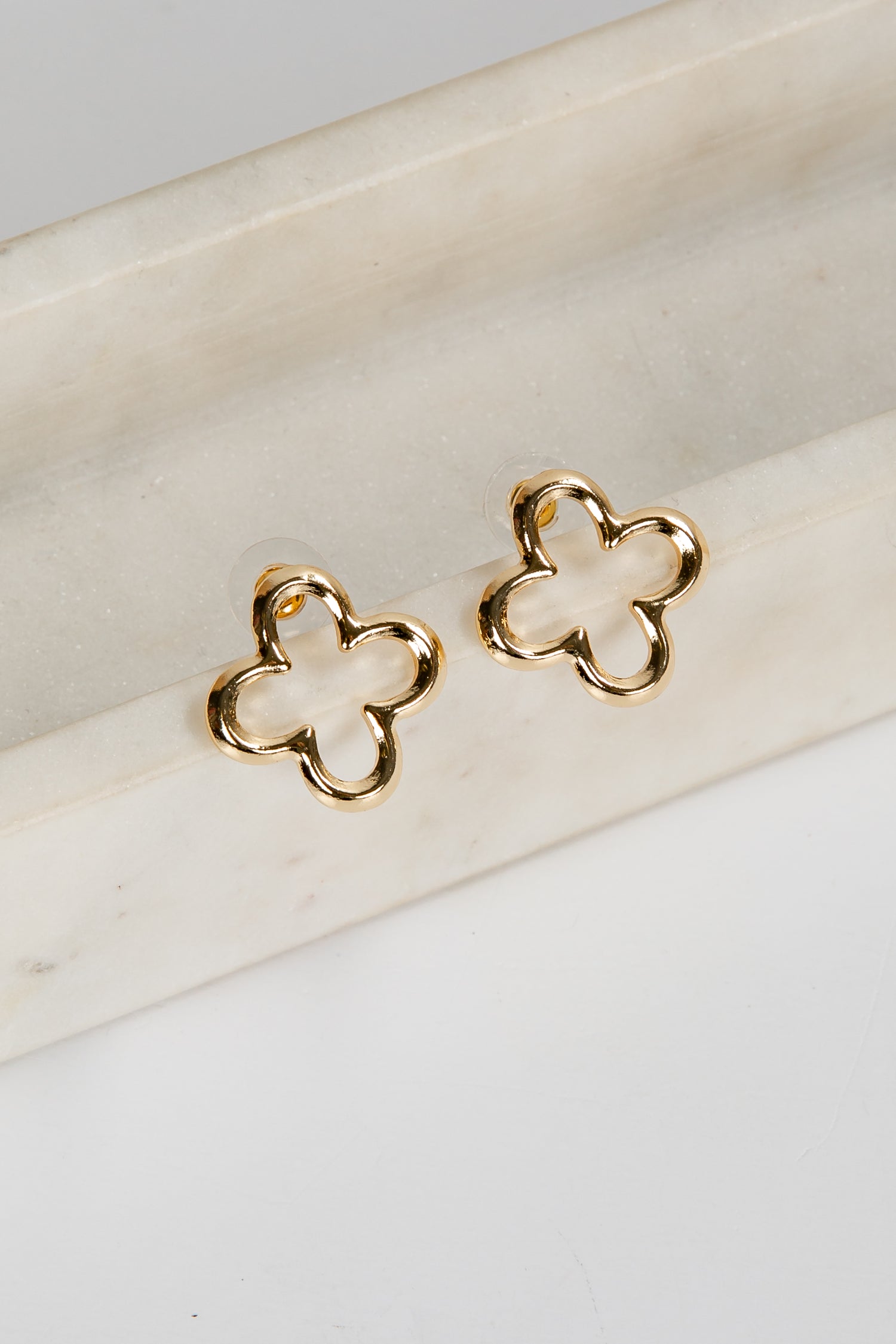 Gold clover-shaped earrings on a white surface