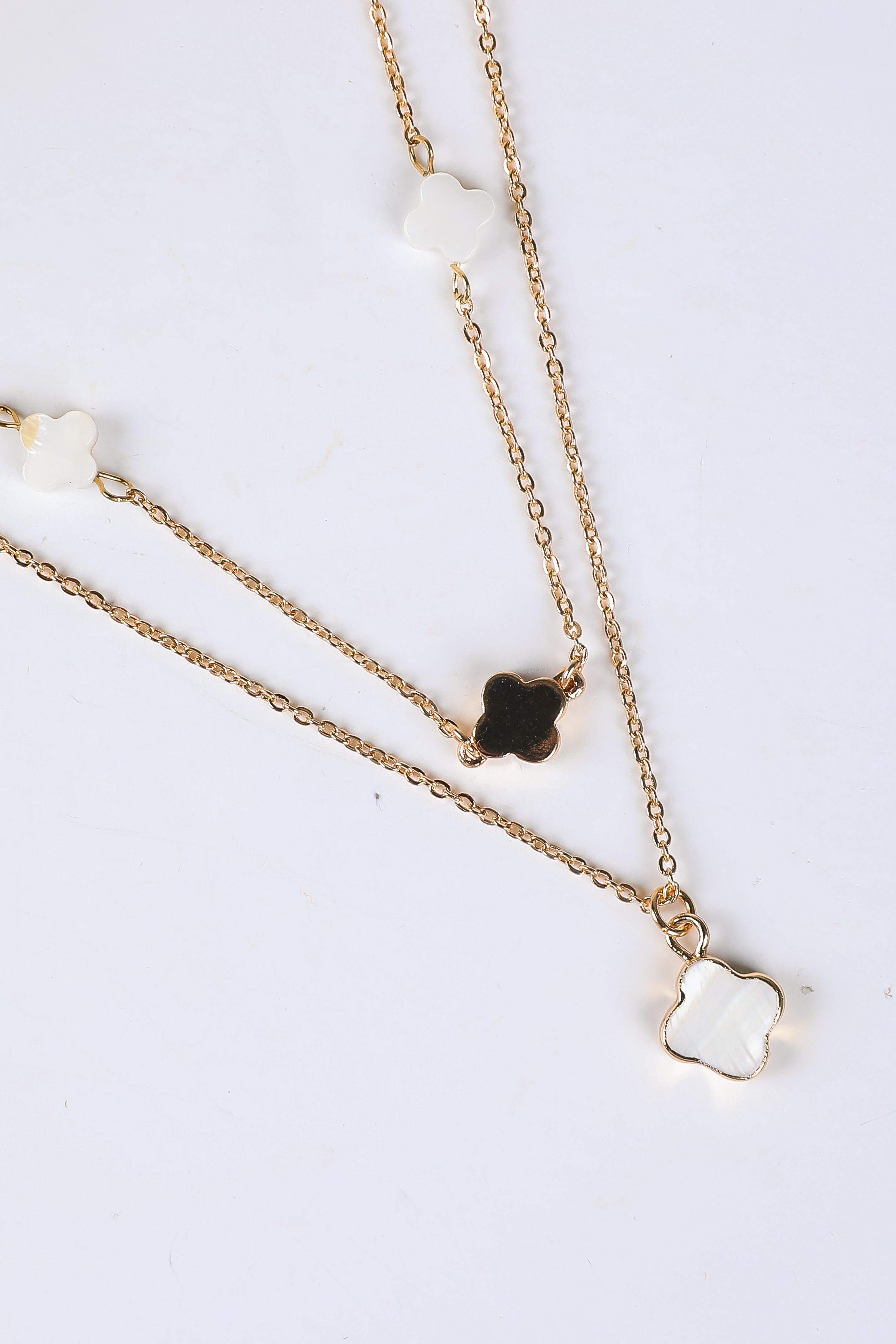 Two gold necklaces with clover pendants on a white background